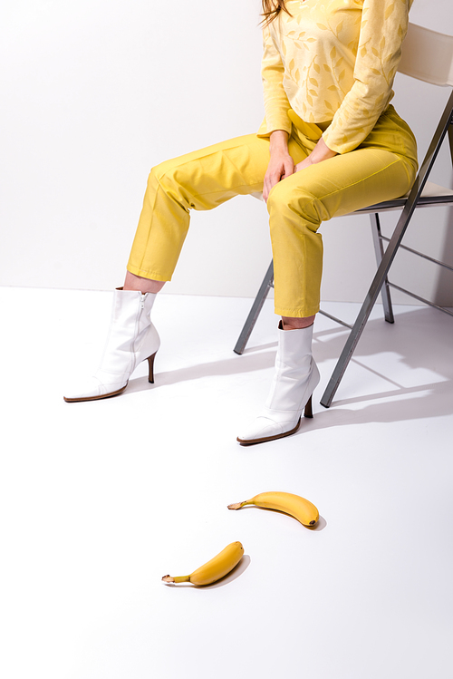 cropped view of woman sitting near yellow bananas on white