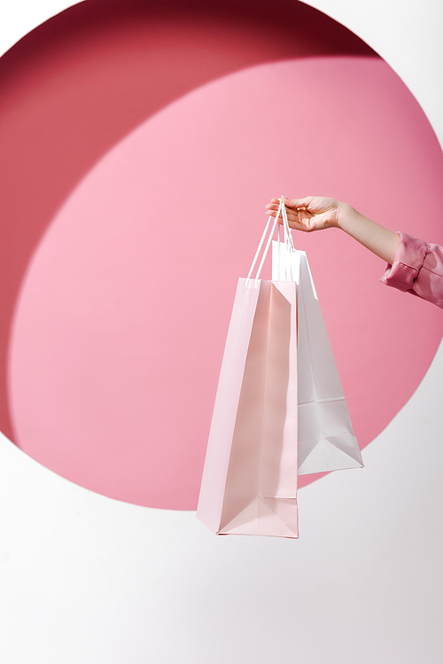 cropped view of woman holding shopping bags on pink and white