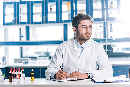 pensive allergist writing in notebook near test tubes with samples