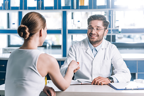 selective focus of happy doctor in glasses shaking hands with woman