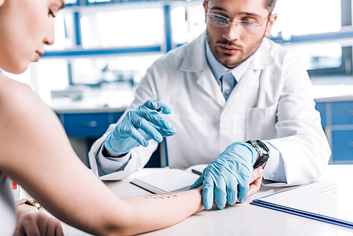 selective focus of allergist in latex gloves holding syringe near attractive woman in clinic