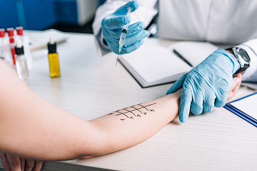 cropped view of allergist in latex gloves holding syringe near woman while doing allergy test in clinic