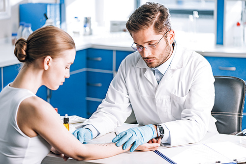 selective focus of handsome allergist holding ruler near marked hand of woman