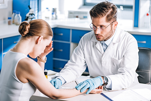 selective focus of handsome allergist holding ruler near marked hand of sad woman