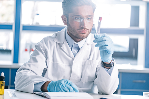 handsome bearded immunologist in glasses looking at test tube