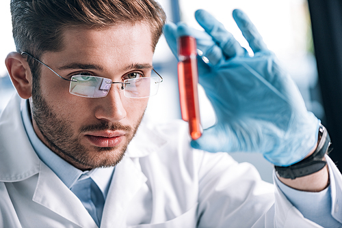 selective focus of bearded immunologist in glasses holding test tube with red liquid