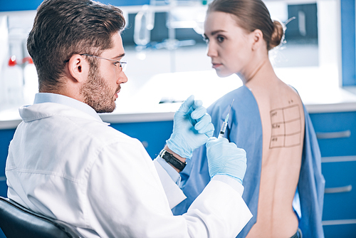 selective focus of handsome allergist holding syringe near patient with letters on marked back