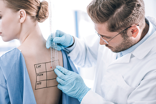 bearded allergist holding ruler near patient with marked back