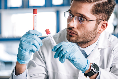 selective focus of bearded immunologist looking at test tubes with letters