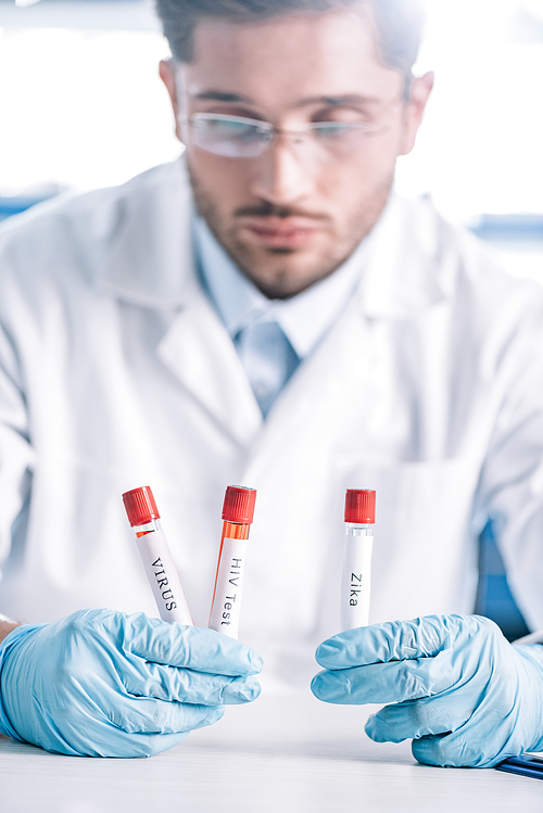 selective focus of bearded immunologist in glasses holding test tubes with letters