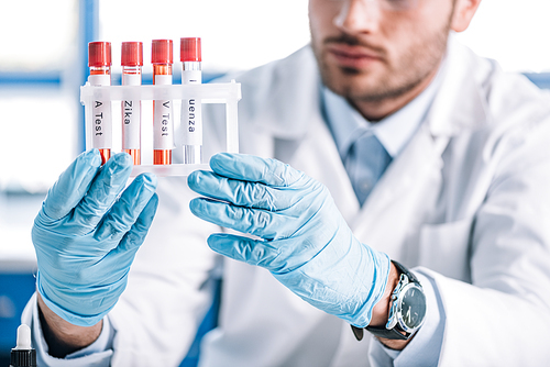 cropped view of bearded immunologist holding test tubes with letters