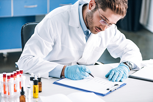 selective focus of bearded immunologist in glasses holding pen near clipboard