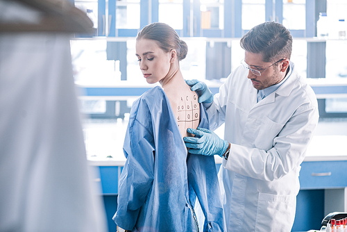 selective focus of allergist standing near attractive woman and touching marked back with numbers and letters