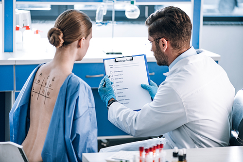 selective focus of allergist holding clipboard near woman with marked back