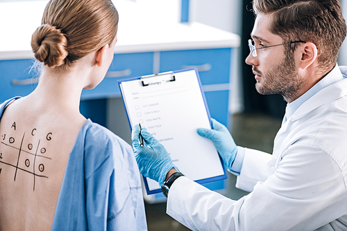 selective focus of handsome immunologist holding clipboard near woman with marked back