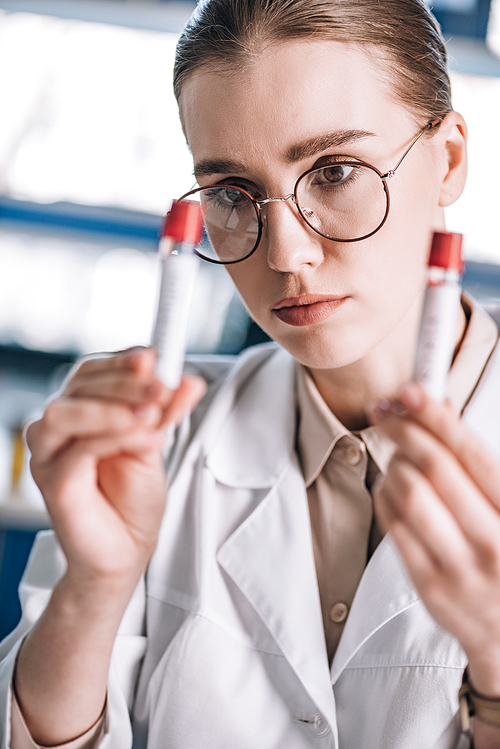 selective focus of beautiful immunologist in glasses looking at test tubes