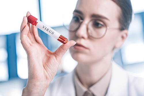 selective focus of immunologist in glasses looking at test tube with virus letters