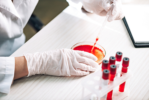 cropped view of immunologist holding pipette with red liquid in laboratory