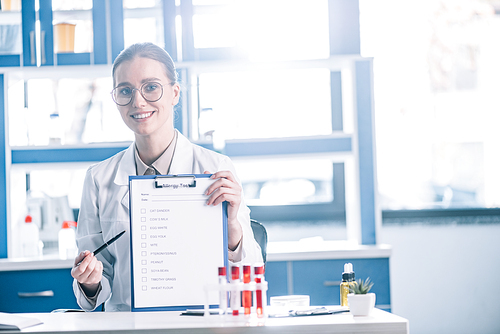 attractive and happy immunologist holding clipboard with checklist and pen