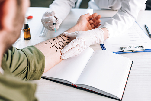 cropped view of allergist holding syringe near man with marked hand