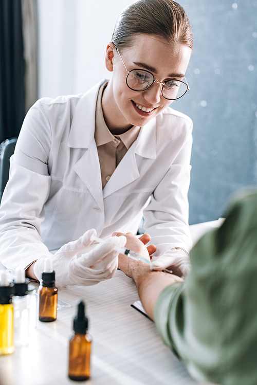 happy allergist holding syringe near man in clinic