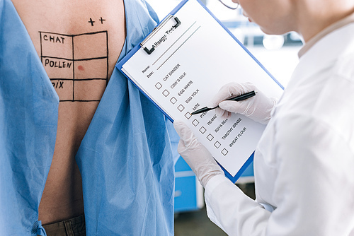 cropped view of allergist holding pen near checklist while holding clipboard near patient