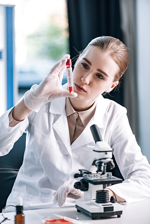 selective focus of attractive immunologist in latex gloves looking at test tube near microscope