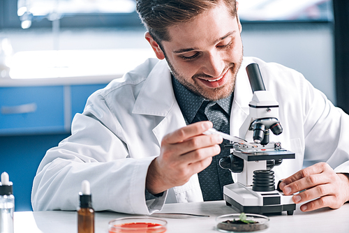 selective focus of happy biochemist with pipette near microscope