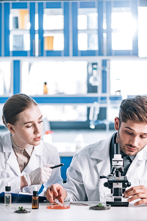 attractive biochemist looking at coworker near microscope