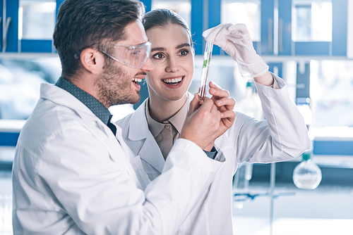 happy biochemists looking at test tube with green plant in laboratory