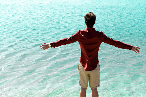 back view of man with outstretched hands standing in turquoise water