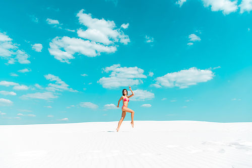 beautiful sexy 20대 여성 in swimsuit jumping on sandy beach with blue sky and clouds