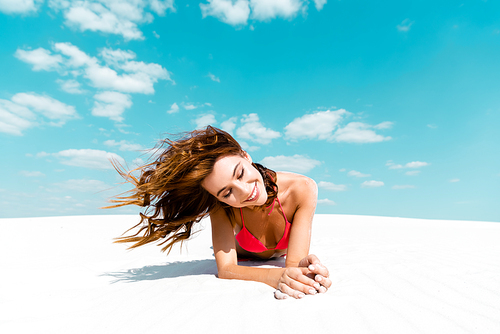 smiling beautiful sexy girl in swimsuit lying on sandy beach with blue sky and clouds at background