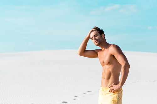 man in swim shorts with muscular torso on sandy beach