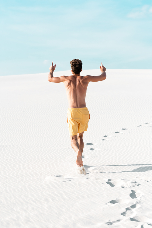 back view of man in swim shorts with muscular torso running on sandy beach