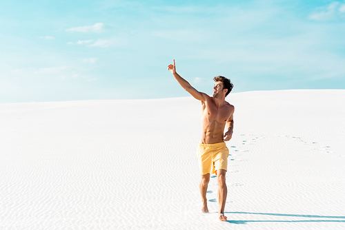 man in swim shorts with muscular torso walking on sandy beach