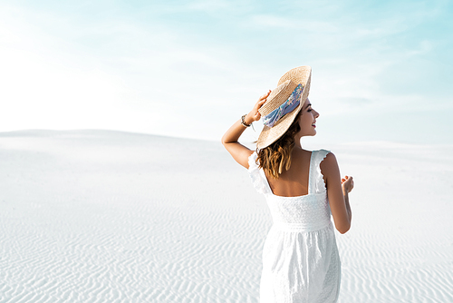 back view of beautiful girl in white dress and straw hat on sandy beach with blue sky