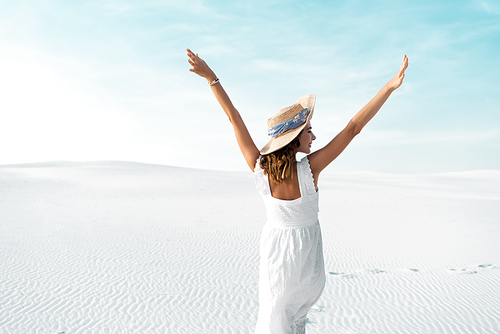 back view of beautiful girl in white dress and straw hat on sandy beach with blue sky