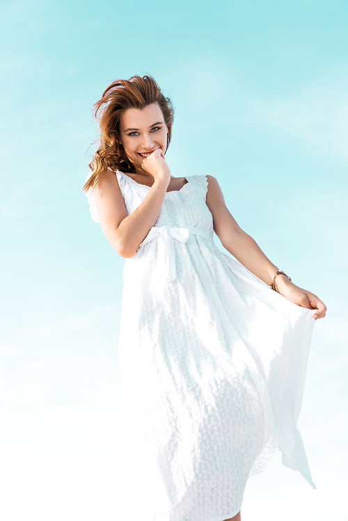 low angle view of smiling beautiful girl in white dress against blue sky