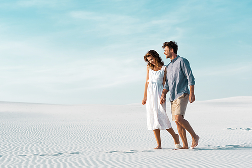 young couple walking on sandy beach against blue sky
