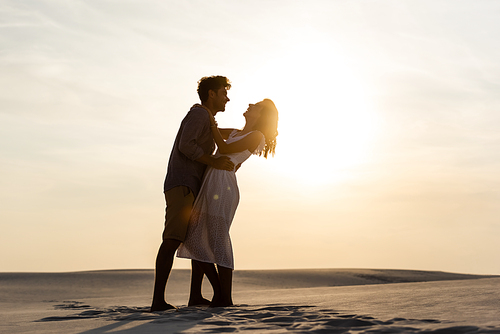 side view of young couple hugging on sandy beach at sunset