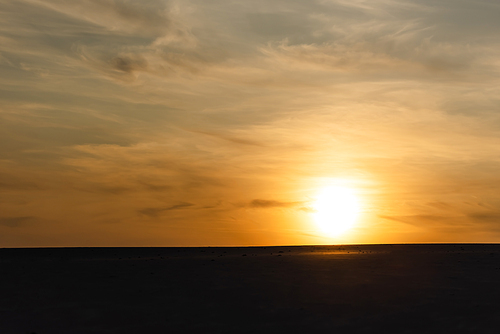 dark sandy beach against bright sun during sunset