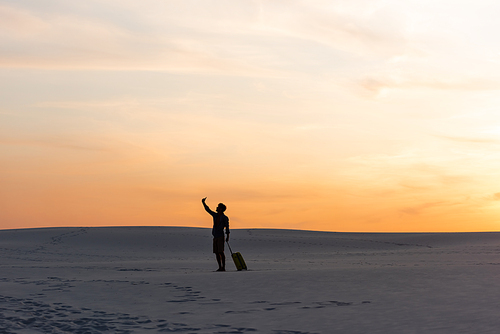 silhouette of man walking on beach with travel bag and smartphone at sunset