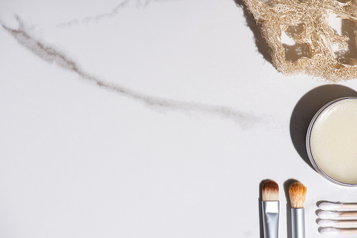 Top view of cosmetic brushes, sponge, jar of wax and ear sticks on white background, zero waste concept