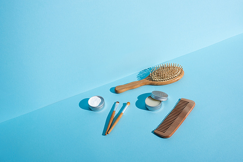 Hair brush, comb, jars of wax and tooth powder, cosmetic brushes on blue background, zero waste concept