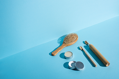 Hair brush, jars of wax and tooth powder, toothbrushes on blue background, zero waste concept
