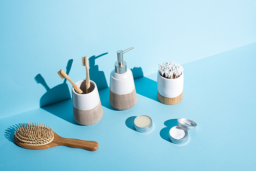 Jars of wax and tooth powder, hair brush, dispenser and toothbrush holders with toothbrushes, ear sticks on blue background, zero waste concept