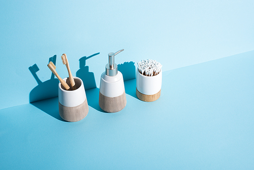 Toothbrush holders with ear sticks and toothbrushes with dispenser liquid soap on blue background, zero waste concept