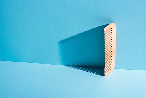 Wooden comb with shadow on blue background, zero waste concept
