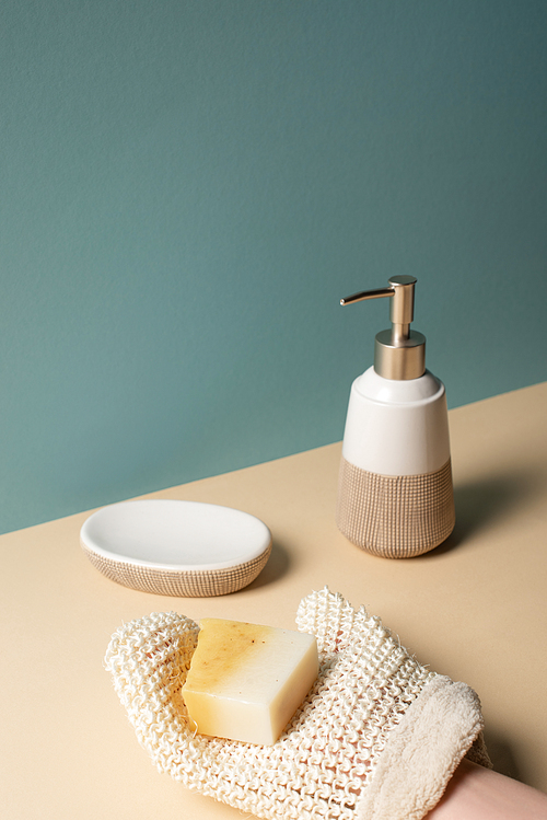 Cropped view of woman holding soap above surface near dispenser, soap dish on beige and grey, zero waste concept